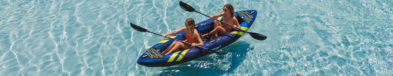 Deux jeunes femmes entrain de pagayer dans un kayak gonflable bleu foncé sur une eau claire.