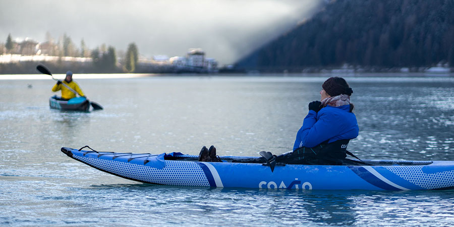 Une femme assise dans son kayak gonflable lotus en bleu dans un lac en suisse en plein Hiver